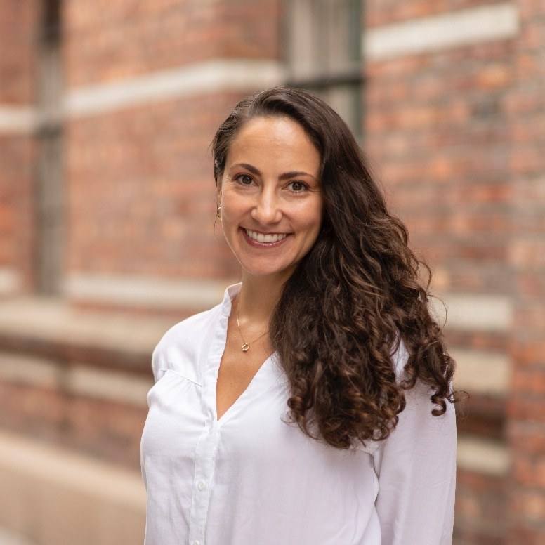 Portrait of Abigail Shemoel in a white shirt against a brick wall